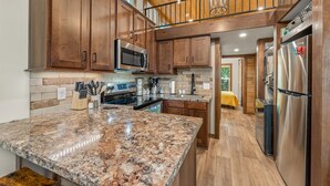 A spacious kitchen with granite countertops, wooden cabinets, stainless steel appliances, and a visible island.