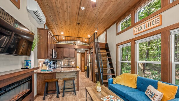 A cozy cabin interior with a kitchen, dining area, and a blue sofa with a 'WELCOME' pillow.