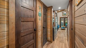 A wooden hallway with a wooden door on the left, a wall-mounted arrow sign, and a view into a room with a blue sofa and a table.