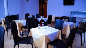 Un espace repas avec plusieurs tables et chaises, un téléviseur fixé au mur et une porte visible au fond.