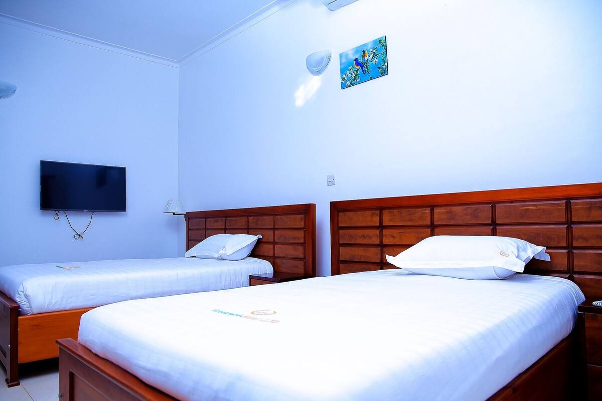 A hotel room with two single beds, a TV, and a painting on the wall.