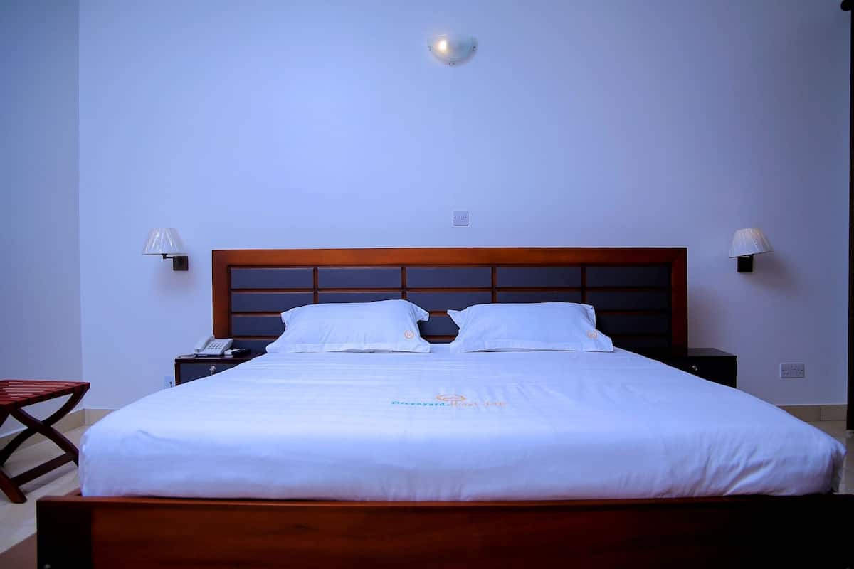 A neatly made bed with white linens and a wooden headboard, a bedside table with a lamp, and a small wooden stool.