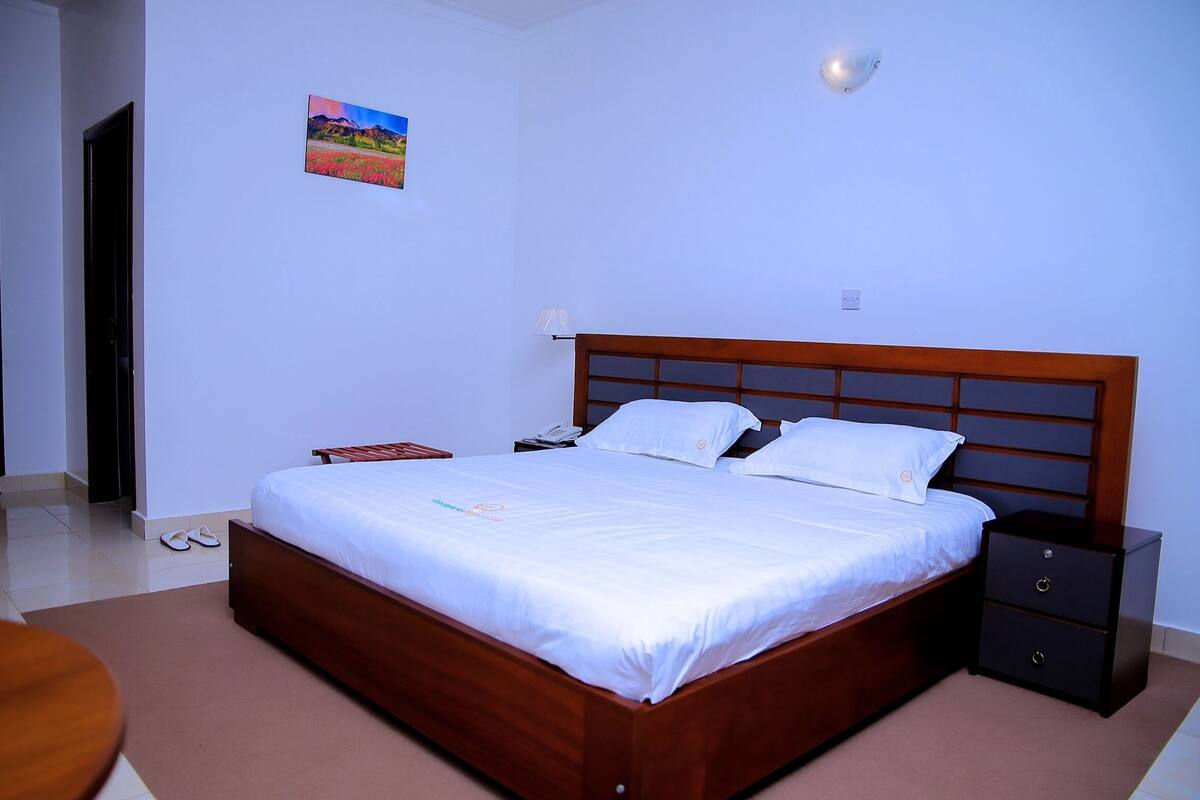 A neatly made bed with white linens, a wooden headboard, and a nightstand with drawers.