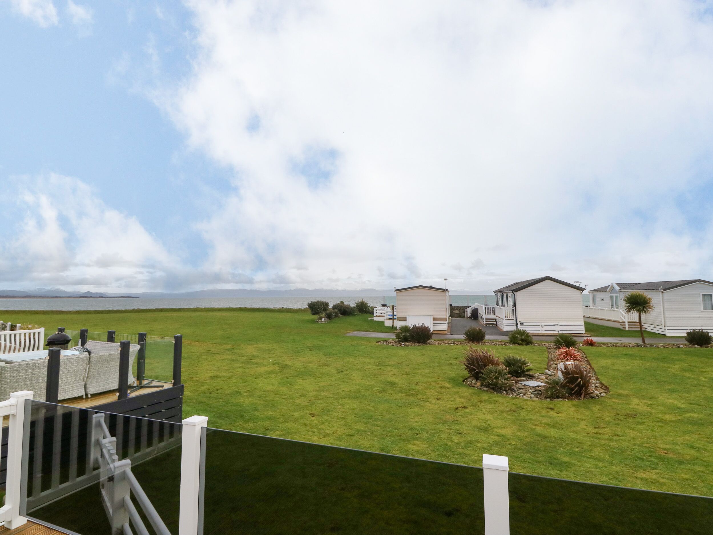 A row of white mobile homes with a grassy field and a clear sky in the background.