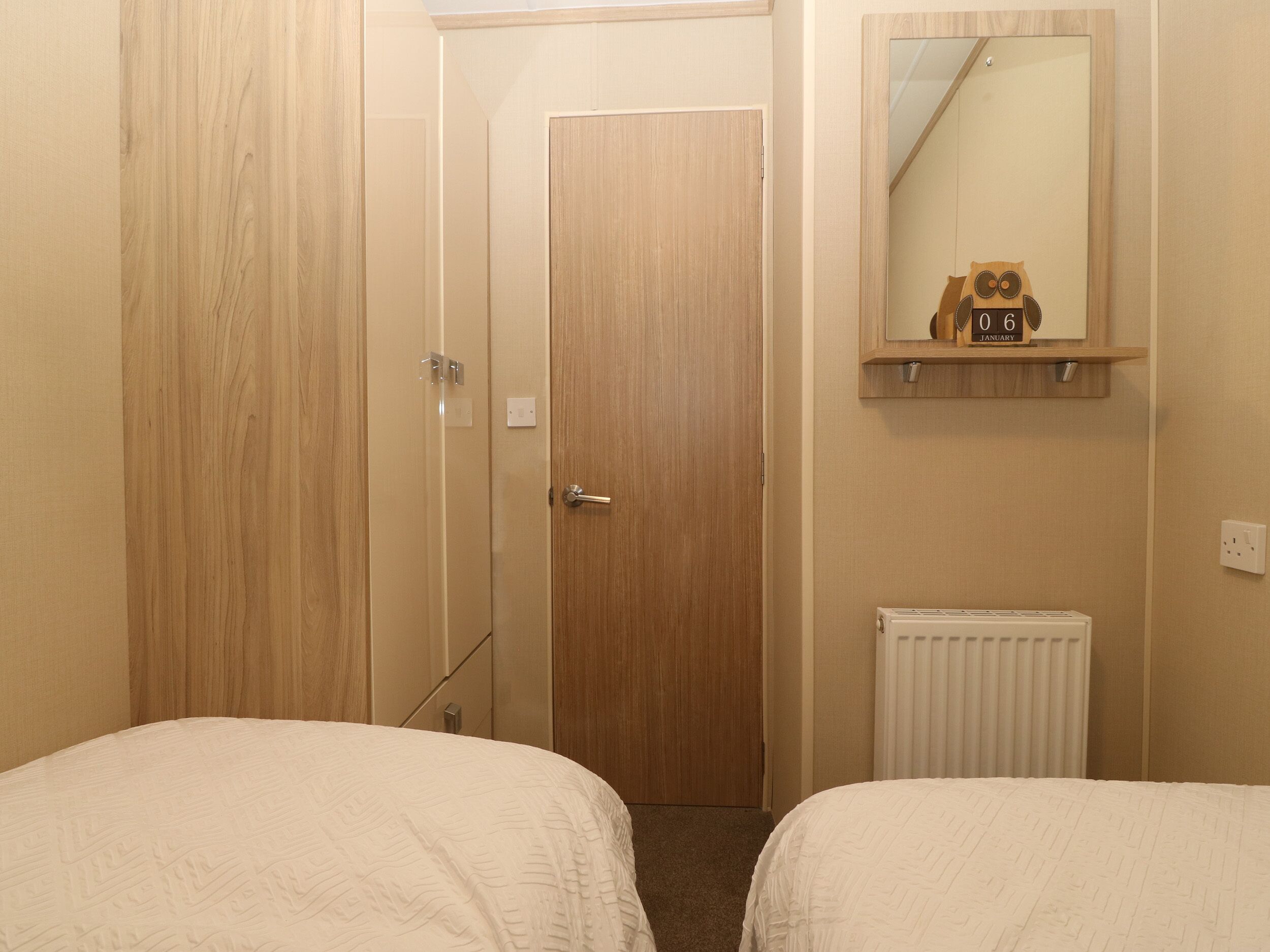 Quarto pequeno e limpo com duas camas, um guarda-roupa de madeira, um espelho e um radiador.