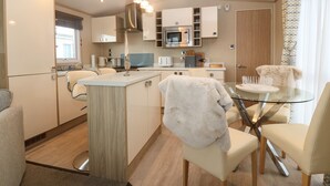 Une cuisine moderne avec des meubles blancs, un îlot central et une table à manger en verre, accompagnée de chaises.