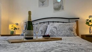 A neatly made bed with a patterned bedspread, a bottle of champagne, and two glasses on a tray.