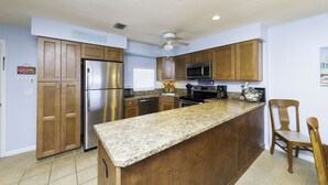 Una cocina con armarios de madera, electrodomésticos de acero inoxidable, encimeras de granito y un ventilador de techo.