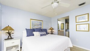 Un dormitorio con cama, mesitas de noche, ventilador de techo e imágenes enmarcadas en la pared.