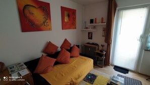 A bedroom with a bed, pillows, a radiator, a shelf with decorative items, and a window with curtains. - Tiny Flat Ferienwohnung in Baiersbronn (Baiersbronn)