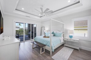 Ein Schlafzimmer mit einem Himmelbett, Deckenventilator, Schreibtisch und einem Fenster mit Jalousien.