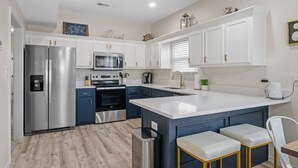 A modern kitchen with white cabinets, stainless steel appliances, and a central island with seating. - Pool/Pickleball and Views! Great Location! (Gulf Shores)