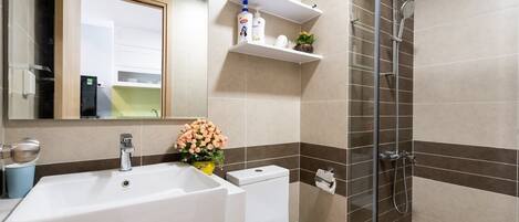 A bathroom with a white sink, toilet, and shower. There are shelves above the sink with toiletries.