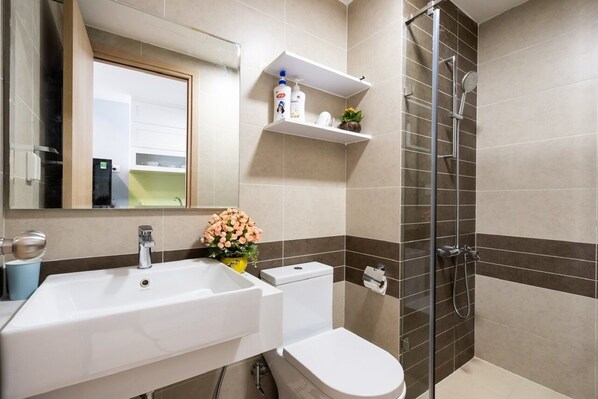 A bathroom with a white sink, toilet, and shower. There are shelves above the sink with toiletries.
