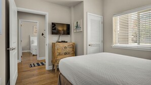 Um quarto com uma cama, cômoda, televisão e janela com persianas.