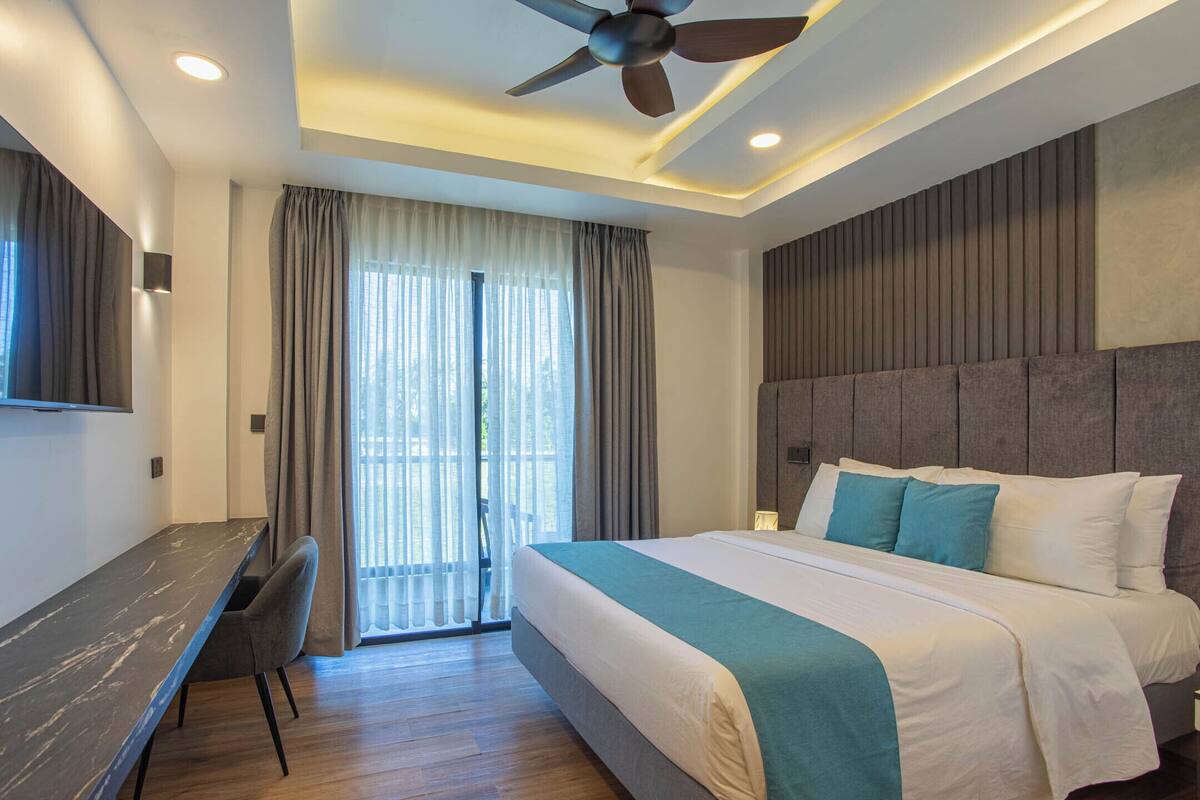 A modern hotel room with a large bed, a desk, and a ceiling fan.