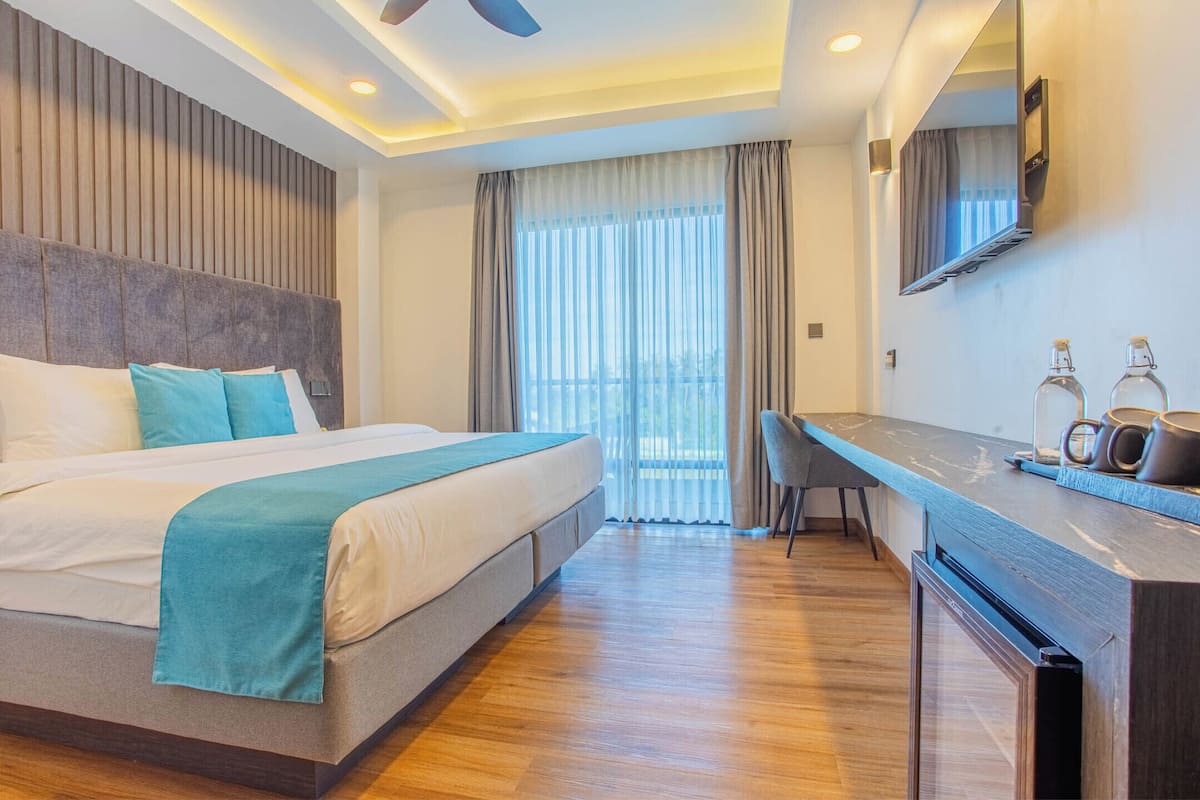 A modern hotel room with a large bed, a desk, and a view of the outdoors.