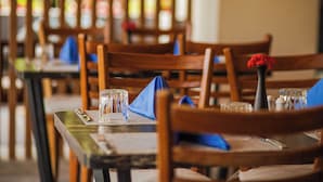 Interior de restaurante con mesas y sillas de madera, algunas con servilletas y copas azules.