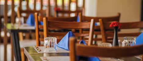 A restaurant interior with wooden tables and chairs, some with blue napkins and glassware.