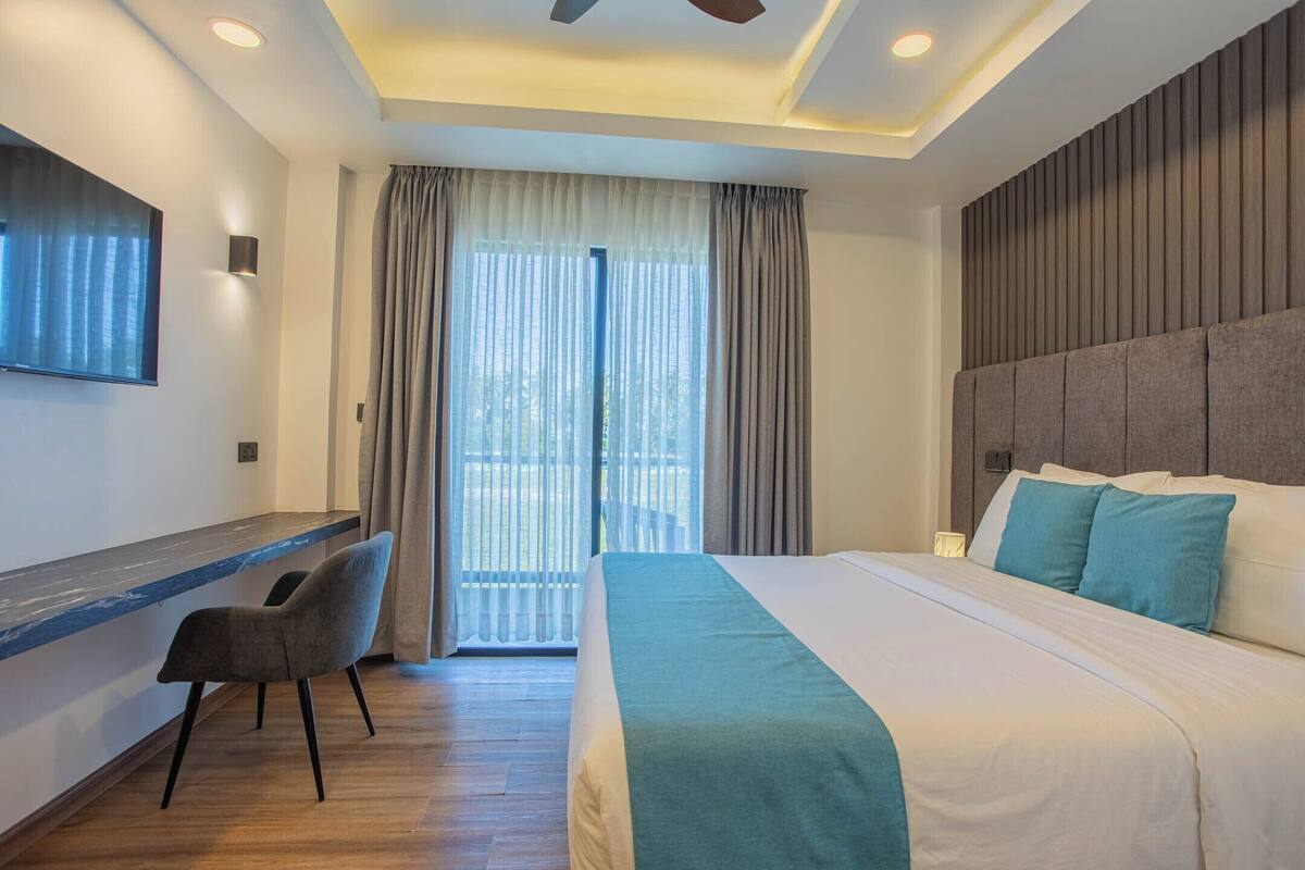A modern hotel room with a large bed, a desk with a chair, a flat-screen TV, and a ceiling fan.