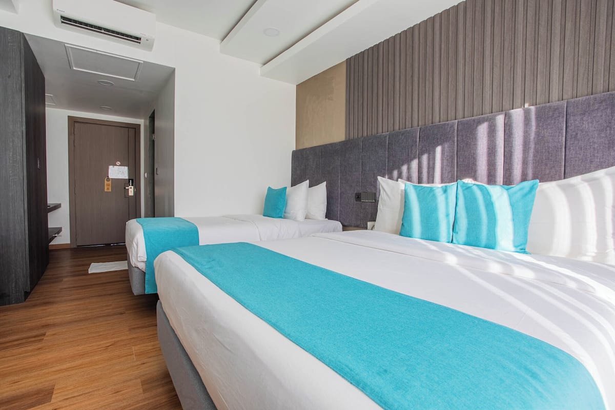 A hotel room with two beds, a wooden floor, a modern headboard, and a door with a light switch.
