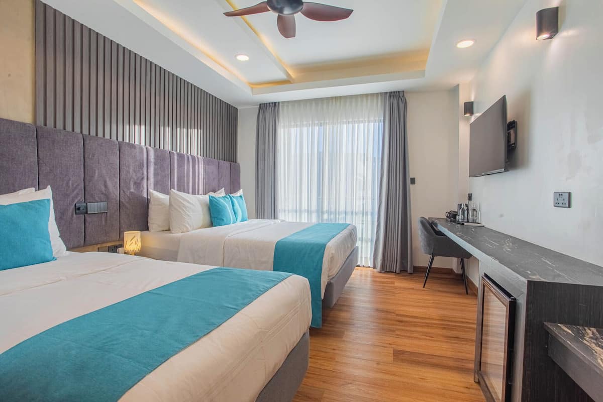 A hotel room with two beds, a desk, a TV, and a ceiling fan.