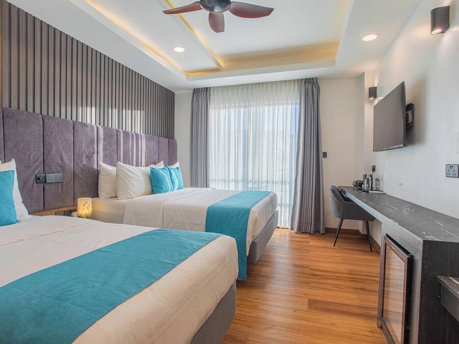 Habitación de hotel con dos camas, un escritorio, un televisor y un ventilador de techo.