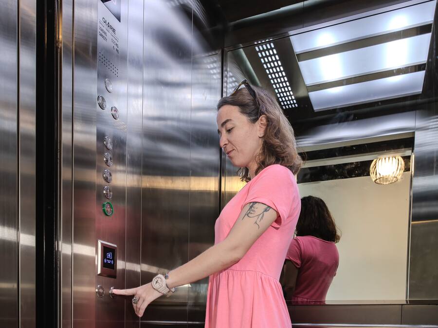 En kvinde i en pink kjole betjener et elevatorkontrolpanel.