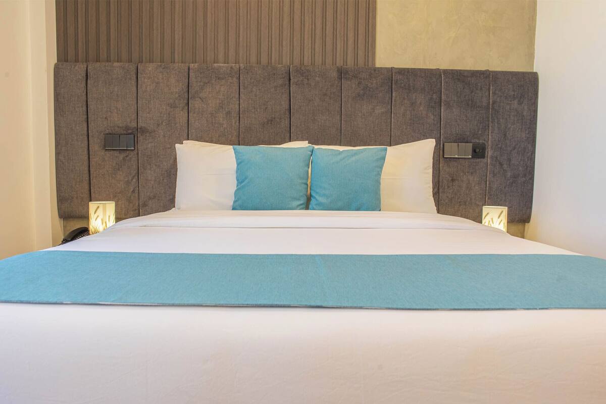A neatly made bed with a grey headboard, white bedding, and a blue accent pillow.