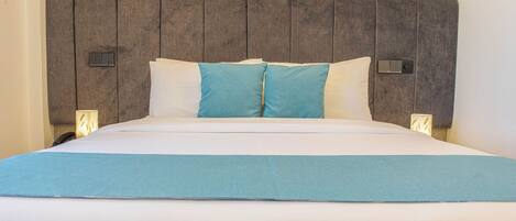 A neatly made bed with a grey headboard, white bedding, and a blue accent pillow.