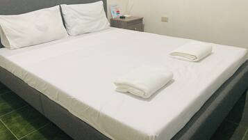 A neatly made bed with white linens and two folded towels on the side.