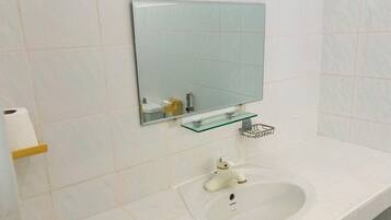 Un baño con lavamanos blanco, un espejo y un dispensador de papel higiénico.
