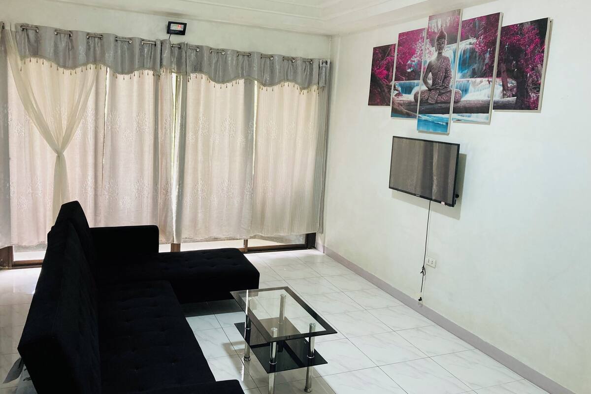 A living room with a black sofa, a glass coffee table, and a flat-screen TV mounted on the wall.