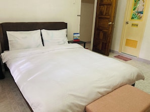A neatly made bed with white linens, a wooden headboard, and a small bedside table with a box.