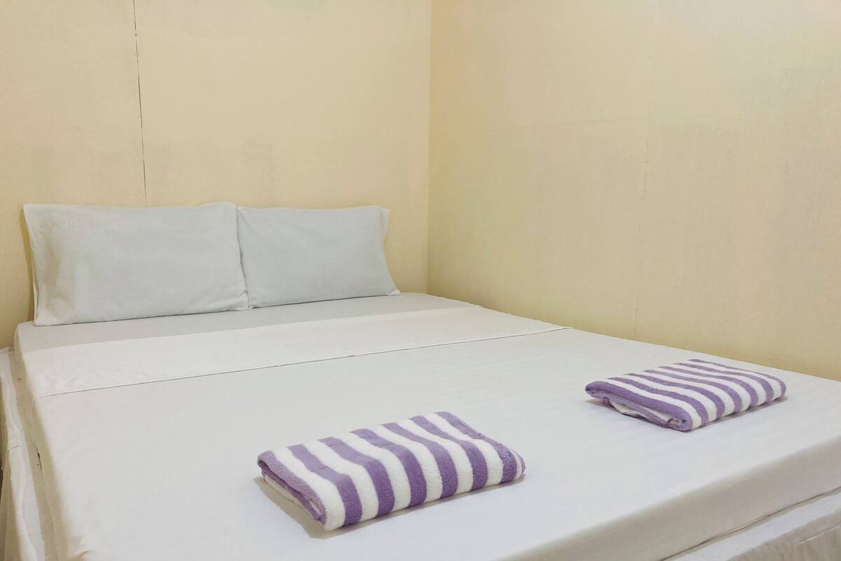 A single bed with white bedding and two purple and white striped towels.