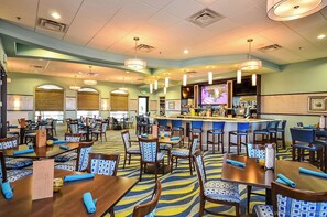A hotel lobby with multiple dining tables, chairs, a bar area, and a television screen. - Resort Access 5BR Oasis w Pool, Game Room near WDW (Kissimmee)