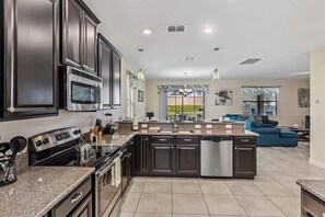 A modern kitchen with dark cabinetry, stainless steel appliances, and a central island. - Resort Access 5BR Oasis w Pool, Game Room near WDW (Kissimmee)