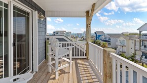 A wooden deck with a white railing, a white chair, and a glass door leading to a shaded area. - Across the Pond | Private Pool + Near Beach (Surf City)