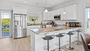 A modern kitchen with white cabinets, stainless steel appliances, and a central island with bar stools. - Across the Pond | Private Pool + Near Beach (Surf City)