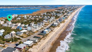 An aerial view of a coastal residential area with houses along the beach, a clear blue sky, and a calm sea. - Across the Pond | Private Pool + Near Beach (Surf City)