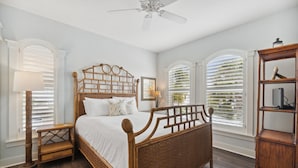 Quarto com cama de madeira, mesa de cabeceira, luminária de chão e estante.