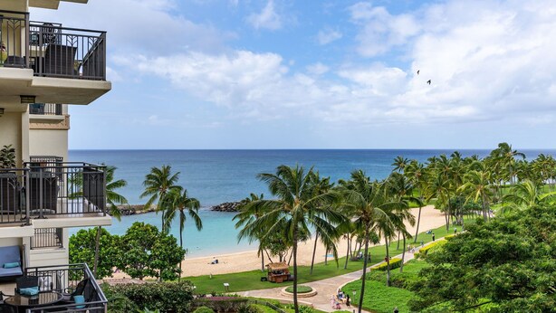 A hotel with a balcony overlooking a beach, palm trees, and a clear view of the ocean.