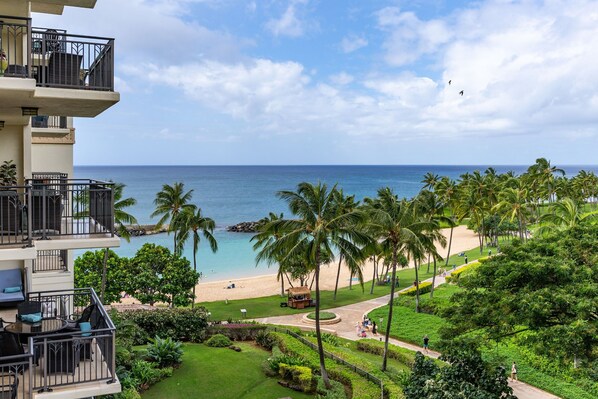 A hotel with a balcony overlooking a beach, palm trees, and a clear view of the ocean.