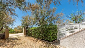 A paved driveway leading to a gated entrance with a white fence and a hedge.