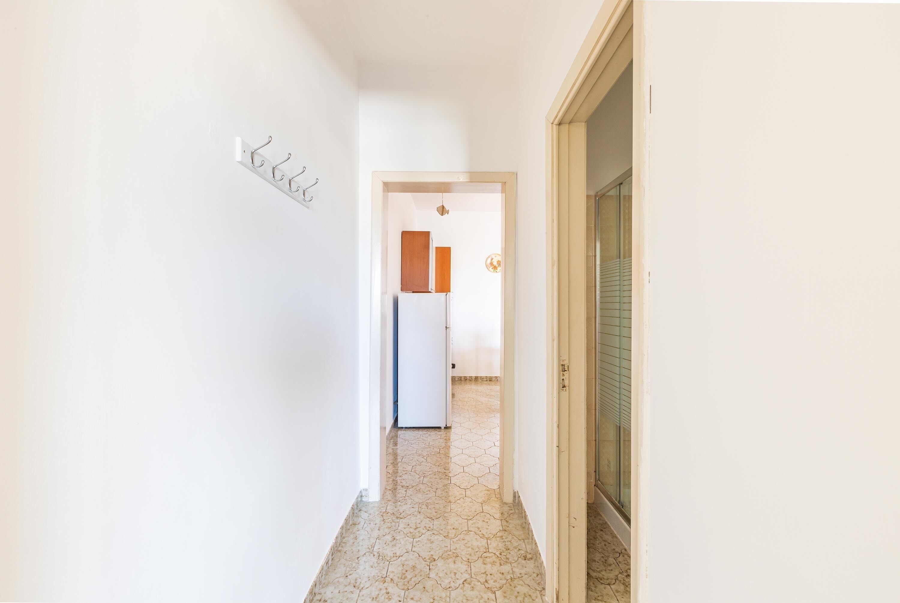 A hallway with a tiled floor, a coat rack, and a door leading to another room.