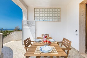 A wooden table set for four with plates, cutlery, and a glass of red wine. A window with a grid pattern is above the table. - 3415 Alba Apartment by Barbarhouse (Porto Cesareo)