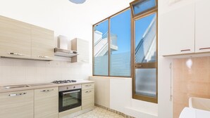 A modern kitchen with light wood cabinets, a gas stove, and a large window providing a view of a building outside.