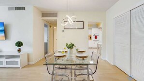 A modern dining area with a glass table and chairs, a pendant light, and a view into the kitchen. - Paradise Retreat: Near Beach, Casino, and More (Hollywood)