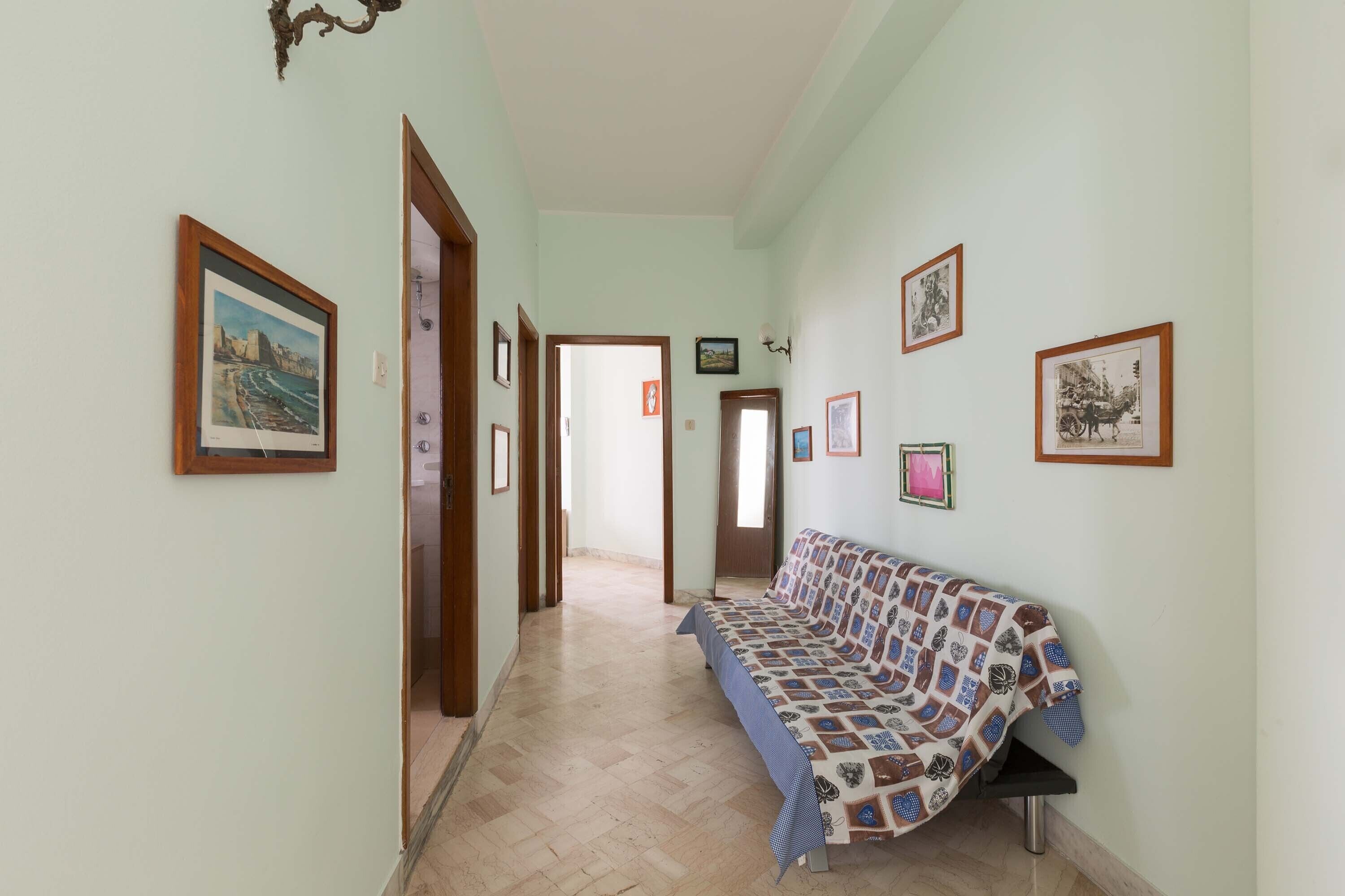 Un couloir avec un canapé, des tableaux encadrés accrochés aux murs et une porte au fond.
