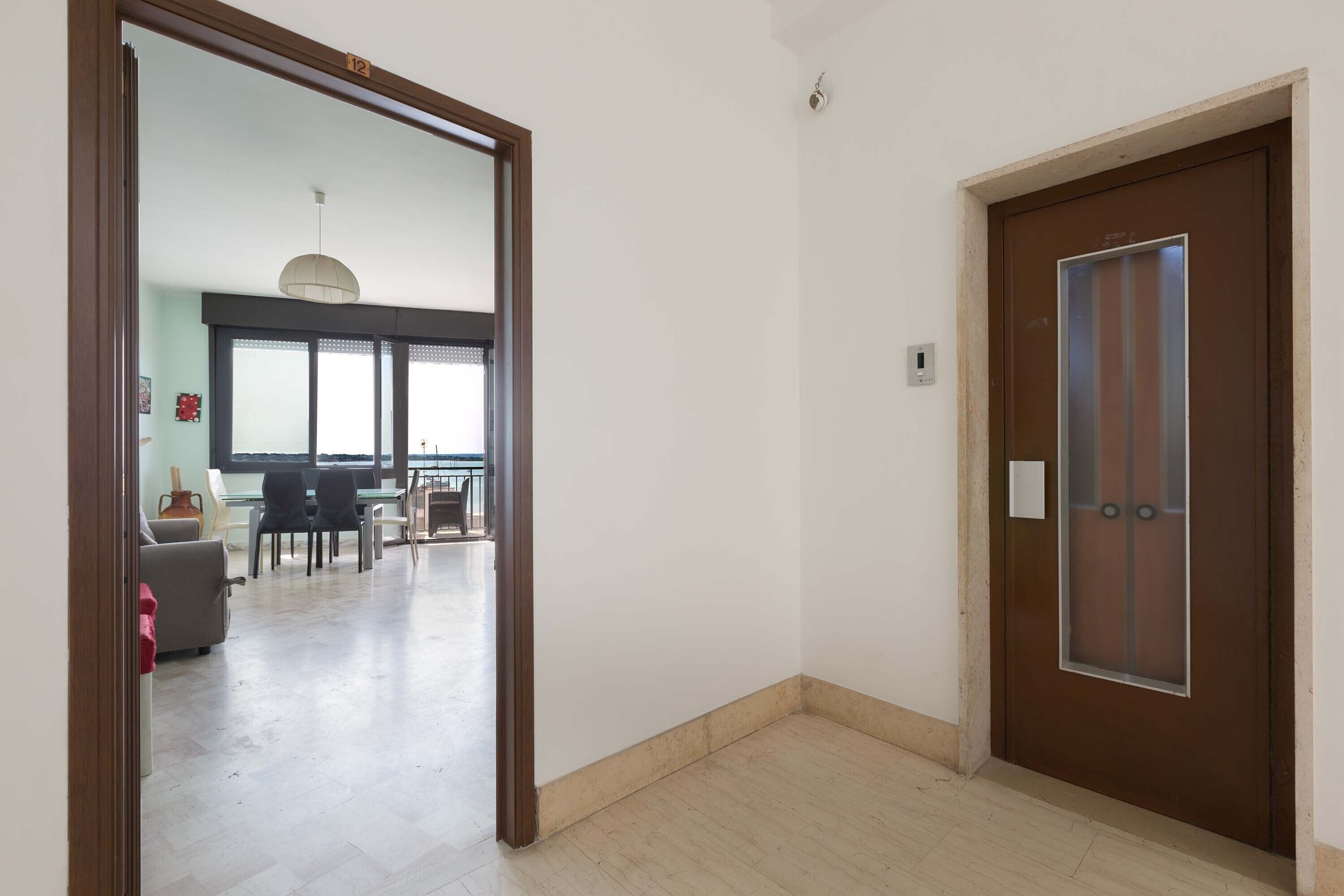 A hallway with a wooden door and a glass door leading to a dining area with a table and chairs.